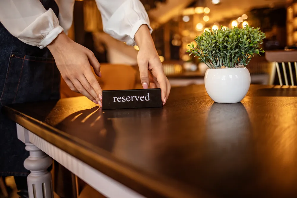With over 80% of diners preferring to book online, restaurant reservation systems are an expected convenience for modern dining. This image shows a member of a restaurant's waiting staff placing a 'reserved' sign on a table in a restaurant.